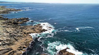 Canlı mavi okyanus dalgalarıyla kusursuz bir şekilde harmanlanan kayalık kıyıların nefes kesici hava manzarasını deneyimleyin.