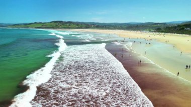 Yuvarlanan dalgalar ve güneş banyosuyla dolu canlı bir sahilin havadan görünüşü, rahatlama ve eğlence için mükemmel bir gün.
