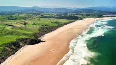 Canlı manzaralar ve kıyıya vuran berrak okyanus dalgalarıyla çevrili çarpıcı bir plajın havadan çekilmiş görüntüsü.