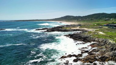 Açık gökyüzünün altındaki kayalık kıyılara çarpan dalgalarla sahilin nefes kesici güzelliğini yakalayın.