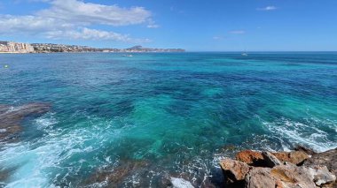 Parlak mavi okyanusun berrak, güneşli bir gökyüzünün altında kayalık kıyı şeridi ile buluşmasının nefes kesici, nefes kesici bir görüntüsü.
