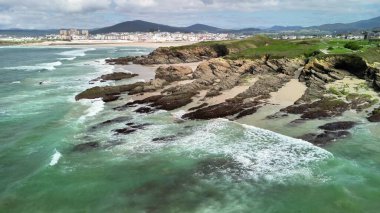 Engebeli bir kıyı şeridinin çarpıcı bir hava manzarası. Turkuaz suları akıyor ve yavaşça kıyıya çarpıyor.