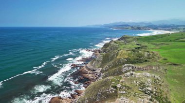 Berrak bir gökyüzünün altında canlı mavi okyanusla birleşen yemyeşil uçurumların çarpıcı hava manzarasını tecrübe edin.