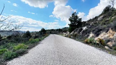 Güzel bir çakıl yolu bulutlarla dolu mavi bir gökyüzünün altında, pitoresk manzaralar arasında yol alır.