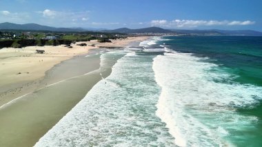 Nazik dalgaların, pırıl pırıl mavi denizin ve yemyeşil yeşilliğin olduğu el değmemiş bir plajın çarpıcı hava manzarasına bakın.