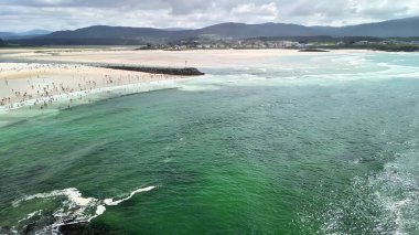 Canlı bir sahilin nefes kesen manzarası berrak suları ve güneşin tadını çıkaran güneşlenenleri gösteriyor..