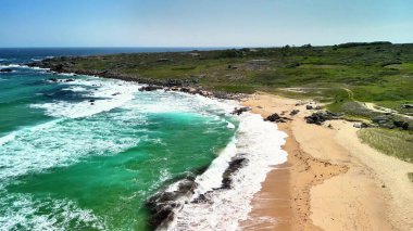 Nefes kesici bir hava manzarası, kristal berrak turkuaz sular ve kayalık bir kıyı şeridinin yer aldığı çarpıcı bir sahili gösteriyor.