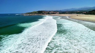 Dalgaların berrak mavi gökyüzünün altında sakin bir plaja çarptığı nefes kesici hava manzarasını deneyimleyin.