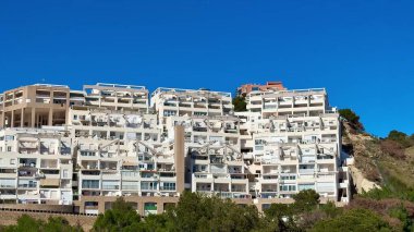 Berrak mavi gökyüzünün altında modern evlerle dolu nefes kesici manzaralı bir tepe manzarası.