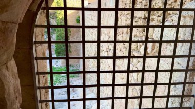 Büyüleyici bir taş pencere. Karmaşık bir metal ızgarayla çerçevelenmiş. Dışarıdaki yemyeşil manzarayı gözler önüne seriyor.