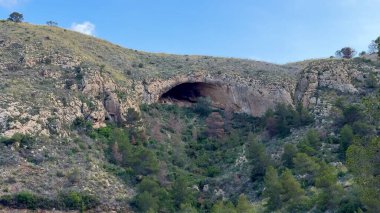 Bir dağ mağarasından nefes kesici bir manzara keşfedin, yemyeşil yemyeşil ve geniş mavi gökyüzü arasında yuva yapmış.
