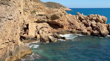 Huzurlu, sakin bir kıyı manzarası sakin ve çarpıcı mavi okyanus sularının yanında kayalık uçurumlar sergiliyor.