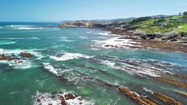 Sersemletici hava görüntülerinde sakin sahil şeridi, canlı mavi su ve parlak güneşli bir günde kayalık kıyılar sergileniyor.