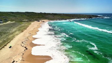 Canlı turkuaz suları ve yumuşak altın kumlarıyla nefes kesici güzel bir sahili gösteren bir hava manzarası.