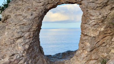 Sakin ve huzurlu denizin çarpıcı manzarası gün batımında doğal bir kaya kemeri tarafından güzel çerçevelenmiştir.