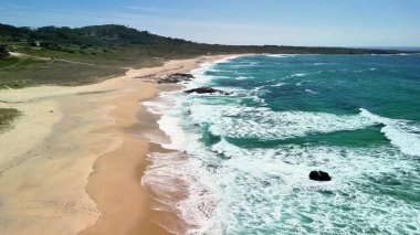 Yumuşak dalgalar ve etrafını saran yemyeşil tepelerle sakin bir plajın nefes kesici manzarasının tadını çıkar.