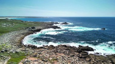 Okyanus dalgalarının nefes kesen görüntüsü berrak mavi gökyüzünün altında kayalık kıyılara çarpıyor.