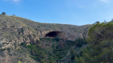 Yeşillik ve görkemli kayalık tepelerle çevrili büyüleyici ve nefes kesici bir mağara manzarası.