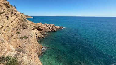 Nefes kesici bir manzara, turkuaz suların engebeli kayalıklara çarptığını gösteriyor. Bu gerçekten sakin kıyı manzarası içinde.