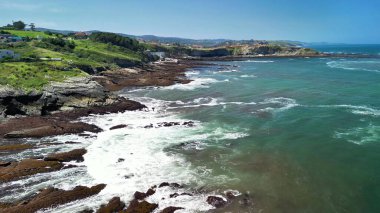 Çarpıcı sahil şeridinde kayalık kıyılara vuran dalgalar var, yemyeşil tepeler güzel bir zemin görevi görüyor.