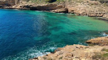 Engebeli kayalıklarla sarmalanmış canlı turkuaz suları gösteren nefes kesici bir kıyı manzarası deneyimleyin.