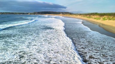 Büyüleyici hava manzarası, yumuşak okyanus dalgalarının güzel kumlu bir sahile ritmik bir şekilde çarptığını gösteriyor.