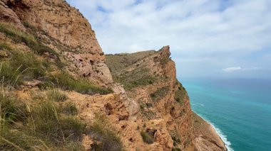 Bulutlu bir gökyüzünün altında dramatik uçurumlara mükemmel bir şekilde kurulmuş canlı turkuaz suların çarpıcı manzarasını deneyimleyin.