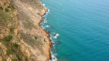 Sakin mavi sularla buluşan kayalık kıyı şeritlerinin çarpıcı manzarasını tecrübe edin. Güzellik arayan doğa aşıkları için mükemmel.