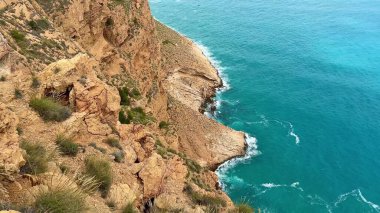 Nefes kesici uçurumlar dramatik bir şekilde yükselir, sakin turkuaz okyanus dalgalarıyla karşılaşır bulutlu bir gökyüzünün altında usulca yuvarlanır