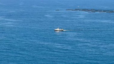 Zarif bir tekne, sakin mavi suların üzerinde zahmetsizce süzülüyor, güzel sakin kıyı manzaralarıyla çevrili.