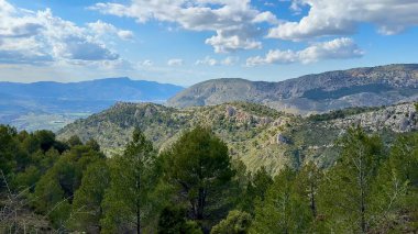 Görkemli dağların büyüleyici panoramik manzarası, yemyeşil yemyeşil ve berrak mavi gökyüzünün altındaki tüylü bulutlar.