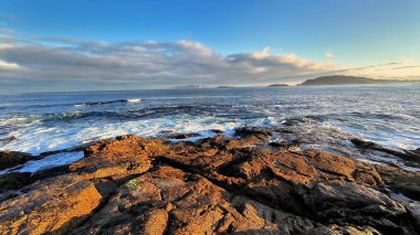 Gün batımında engebeli kayalara çarpan okyanus dalgalarının sakin manzarası, doğa ve seyahat temaları için idealdir.