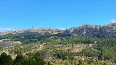 Nefes kesen panoramik manzara, canlı mavi gökyüzünün altındaki yemyeşil yemyeşil, çarpıcı dağlık araziyi gösteriyor.