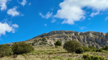 Beraberinde berrak mavi gökyüzünün altındaki yemyeşil bitki örtüsü eşliğinde engebeli dağların nefes kesici ve büyüleyici manzarası.