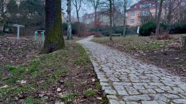 Huzurlu, dolambaçlı bir kaldırım taşı yolu, bereketli doğayla çevrili sakin bir park ortamında usulca dolanıyor.
