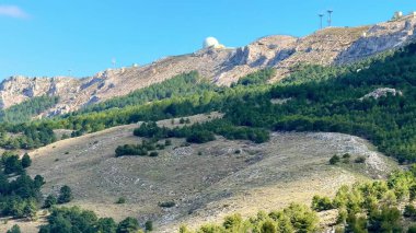 İletişim kuleleri ve çevresini çevreleyen canlı yeşillikle görkemli dağların çarpıcı bir manzarası var.