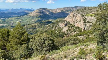 Nefes kesici manzara kayalık tepeleri, yemyeşil vadilerin yanında sergiliyor, hepsi yukarıdaki parlak mavi gökyüzünün altında.