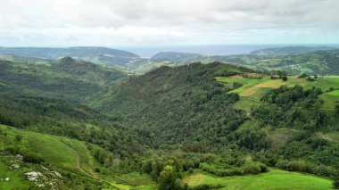 Göz kamaştırıcı bir panoramik manzara güzel bir şekilde canlı tepeler, yemyeşil yemyeşil ve sakin bir okyanus arkaplanı sergiliyor.