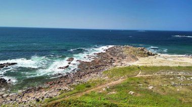 Kayalık bir kıyı şeridinin ve güzel okyanusun güneşli gününde dalgaların tadını çıkar.