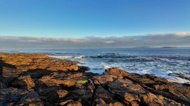 Engebeli, görkemli kayalar ve açık mavi bir gökyüzünün altında hafif dalgaların yer aldığı güzel, sakin bir deniz manzarası.