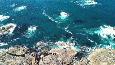 Engebeli kayalara çarpan canlı okyanus dalgalarını güzel gösteren nefes kesici bir hava manzarası.