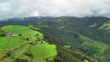 Nefes kesen hava manzarası yuvarlanan yeşil tepeler ve bulutlu bir gökyüzünün altında manzaralı tarım arazileri..
