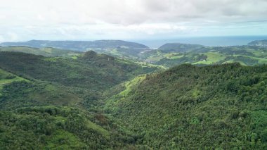 Nefes kesen hava manzarası canlı yeşil tepeleri bulutlu gökyüzünün altında kusursuz bir şekilde okyanusla buluşurken yakalıyor.