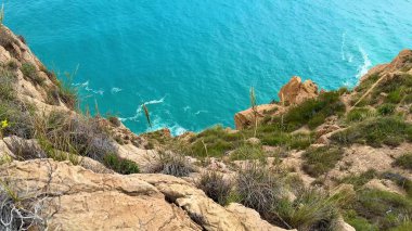 Turkuaz okyanus dalgalarının engebeli kayalıklara çarptığını hissedin. Huzurlu, resimli bir cennette.