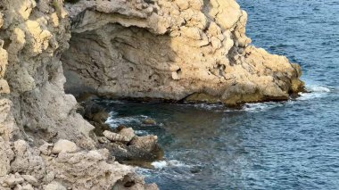 Büyüleyici ve nefes kesici manzara dalgaların yavaşça kıyıya vurduğu engebeli bir kayalık kıyı şeridini gösteriyor.