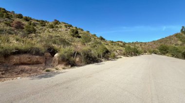 Berrak mavi gökyüzünün altında yemyeşil yemyeşil ile çevrili sakin ve huzurlu bir dağ yolu.