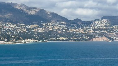 Olağanüstü berrak mavi sular ve pitoresk yeşil tepeler içeren nefes kesici bir kıyı şeridi manzarası.