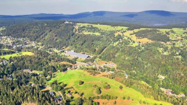 Göz kamaştırıcı bir hava perspektifi, berrak bir gökyüzünün altında uzanan dingin dağların yanında yemyeşil tepeler sergiliyor.