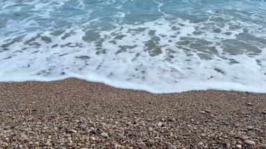 Yumuşak dalgalar hoş, çakıllı bir plaja hafifçe çarpıyor, güzel ve sakin bir sahil atmosferi yaratıyor.