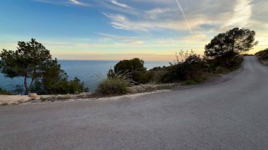 Parlak okyanusun yanındaki sarmal kıyı yolunun çarpıcı manzarası büyüleyici bir gün batımıyla güçlenmiştir.